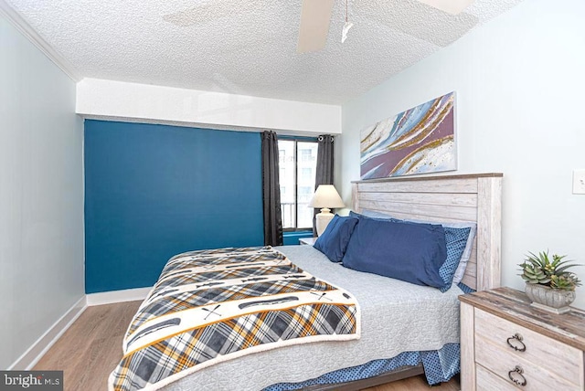 bedroom with a ceiling fan, a textured ceiling, baseboards, and wood finished floors