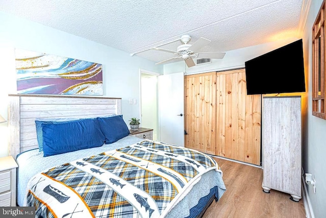 bedroom with wood-type flooring, ceiling fan, a barn door, and a textured ceiling