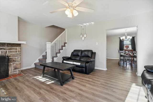 living room with a stone fireplace, hardwood / wood-style floors, and ceiling fan with notable chandelier