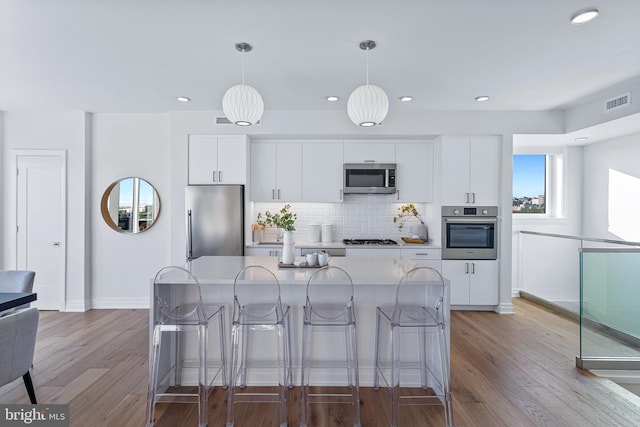 kitchen with stainless steel appliances, white cabinets, light hardwood / wood-style floors, and hanging light fixtures