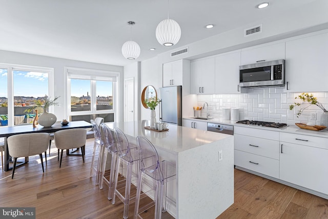 kitchen featuring white cabinets, pendant lighting, stainless steel appliances, a center island, and hardwood / wood-style floors