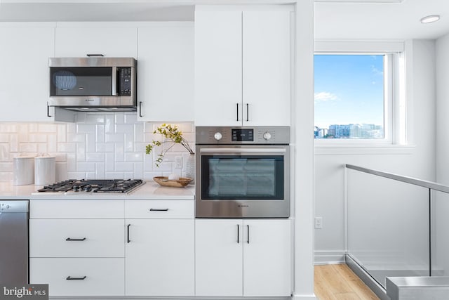 kitchen featuring white cabinets, stainless steel appliances, light wood-type flooring, and tasteful backsplash