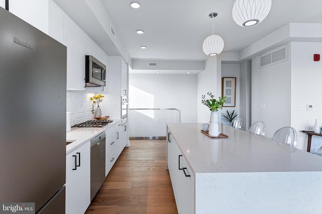 kitchen featuring white cabinetry, hanging light fixtures, a kitchen island, light hardwood / wood-style flooring, and appliances with stainless steel finishes