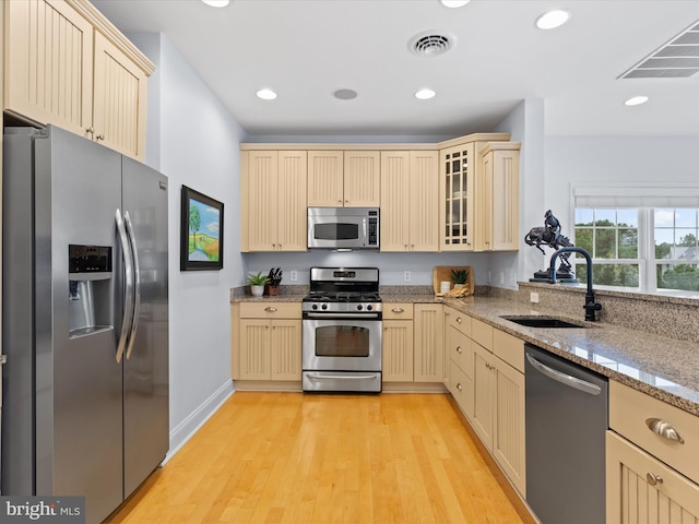 kitchen with light stone countertops, stainless steel appliances, light wood-type flooring, and sink