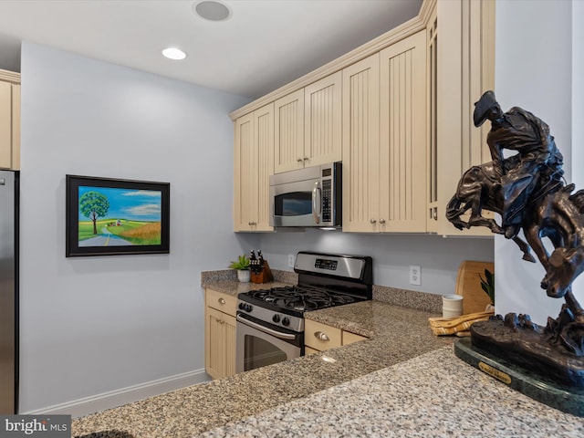 kitchen with light stone counters, appliances with stainless steel finishes, and cream cabinetry