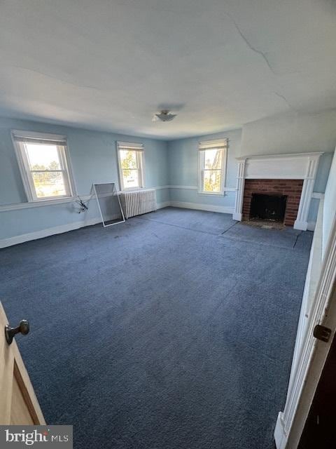 unfurnished living room featuring dark colored carpet, plenty of natural light, and a fireplace