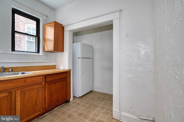 kitchen featuring light countertops, brown cabinetry, a sink, and freestanding refrigerator
