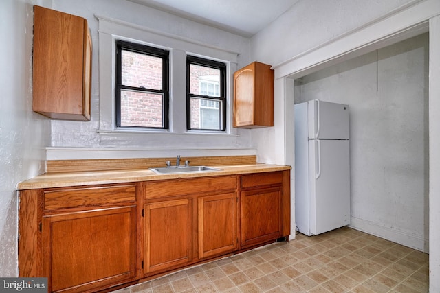 kitchen with freestanding refrigerator, light countertops, a sink, and brown cabinetry