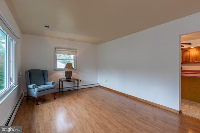 living area featuring light wood-type flooring, baseboard heating, and plenty of natural light