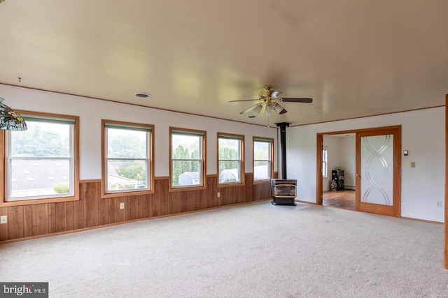 interior space featuring carpet floors, wood walls, ceiling fan, and a wood stove