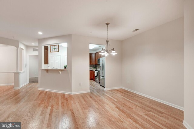 spare room featuring light wood-type flooring and a chandelier