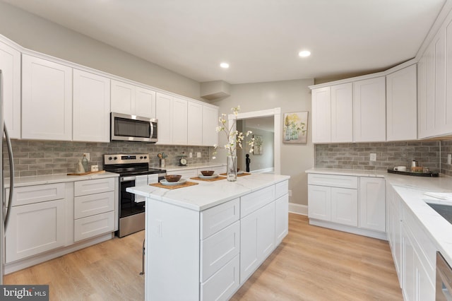 kitchen featuring appliances with stainless steel finishes, white cabinets, light hardwood / wood-style flooring, and tasteful backsplash