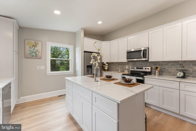 kitchen with an island with sink, stainless steel appliances, white cabinets, and light stone countertops