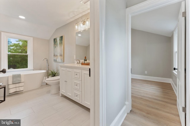 bathroom featuring a bathtub, vaulted ceiling, vanity, toilet, and hardwood / wood-style floors