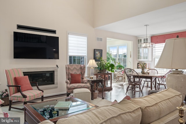 living room featuring a towering ceiling, a notable chandelier, plenty of natural light, and light wood-type flooring