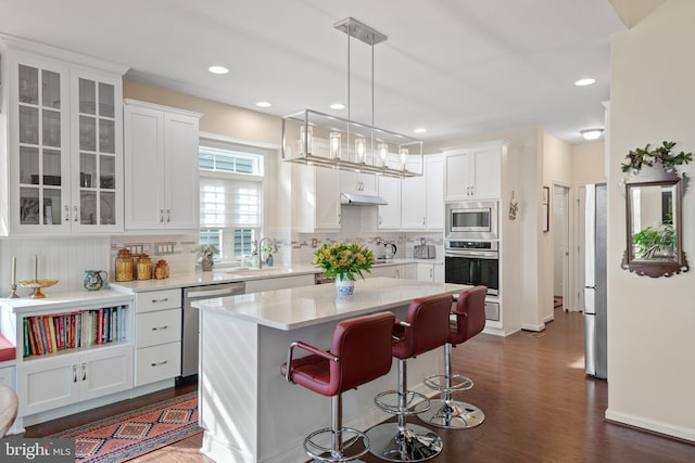 kitchen featuring a kitchen island, stainless steel appliances, decorative light fixtures, white cabinets, and dark wood-type flooring