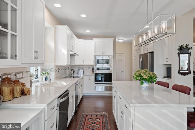 kitchen with white cabinets, a breakfast bar area, stainless steel appliances, decorative light fixtures, and sink