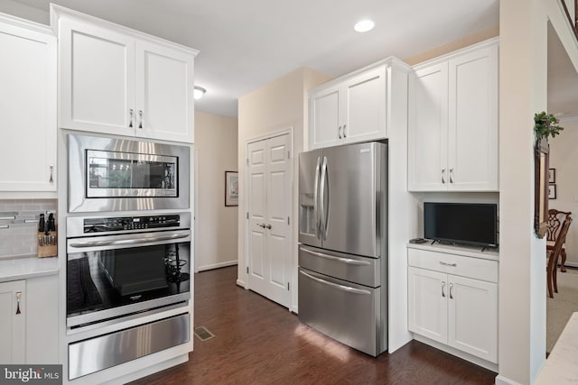 kitchen with appliances with stainless steel finishes, dark hardwood / wood-style floors, white cabinets, and tasteful backsplash