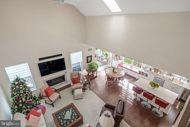 living room with hardwood / wood-style floors, a skylight, high vaulted ceiling, and ceiling fan