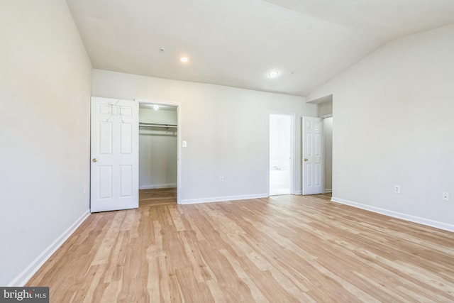 unfurnished bedroom featuring a walk in closet, a closet, light wood-type flooring, and vaulted ceiling