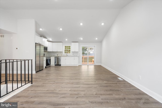 unfurnished living room with high vaulted ceiling, light hardwood / wood-style floors, and sink