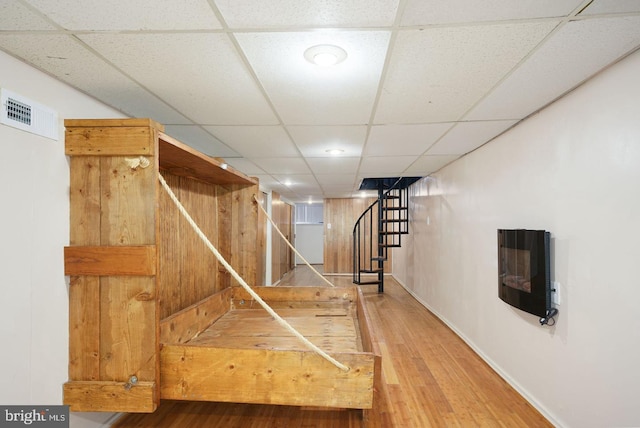 interior space with a paneled ceiling, wooden walls, hardwood / wood-style floors, and heating unit