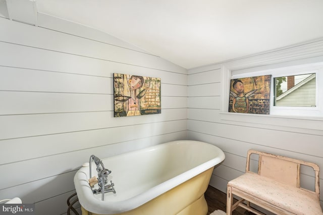 bathroom with lofted ceiling, wood walls, and a bathtub