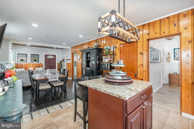 kitchen with a chandelier, a center island, light tile patterned flooring, wood walls, and light stone countertops