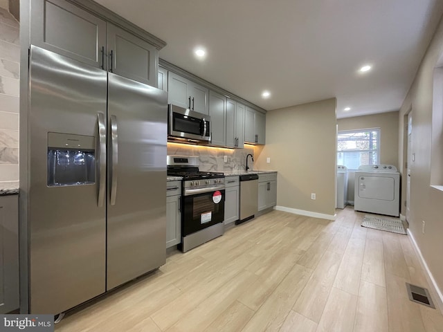 kitchen featuring sink, light hardwood / wood-style flooring, gray cabinets, appliances with stainless steel finishes, and washer and dryer