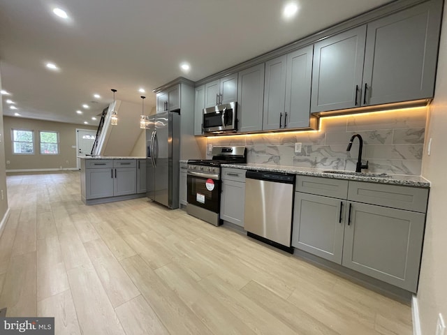 kitchen featuring gray cabinetry, stainless steel appliances, light hardwood / wood-style flooring, and light stone countertops