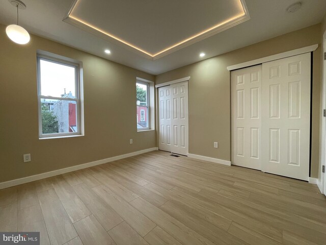 unfurnished bedroom featuring light wood-type flooring, two closets, and multiple windows