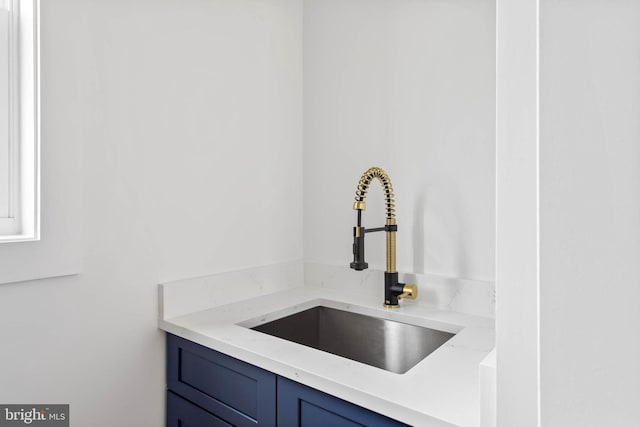 interior details with blue cabinetry, sink, and light stone counters