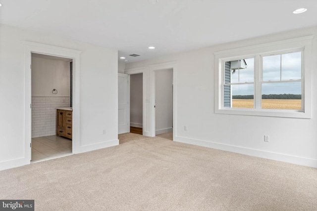 unfurnished bedroom featuring ensuite bath and light colored carpet