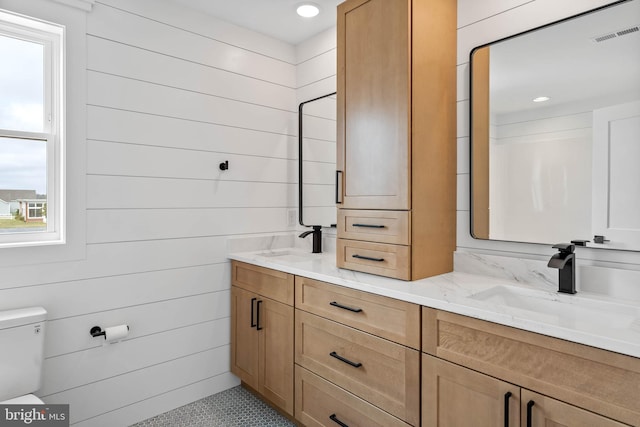 bathroom featuring vanity, wooden walls, toilet, and plenty of natural light