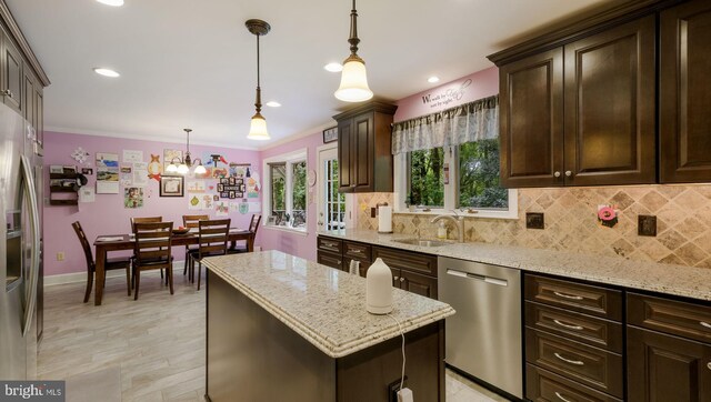 kitchen with light stone counters, hanging light fixtures, sink, a kitchen island, and stainless steel appliances