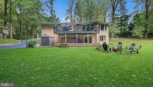 rear view of house with a storage shed, a yard, and a fire pit