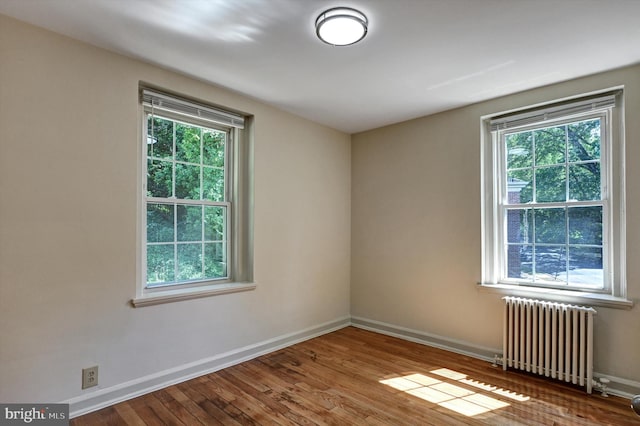 unfurnished room featuring hardwood / wood-style flooring, plenty of natural light, and radiator heating unit