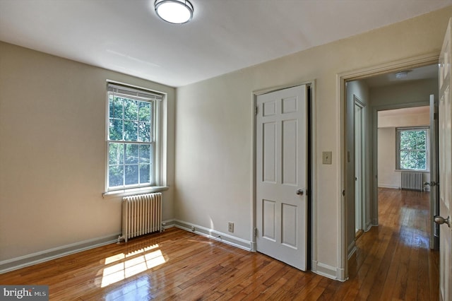 unfurnished bedroom featuring multiple windows, radiator, and hardwood / wood-style floors