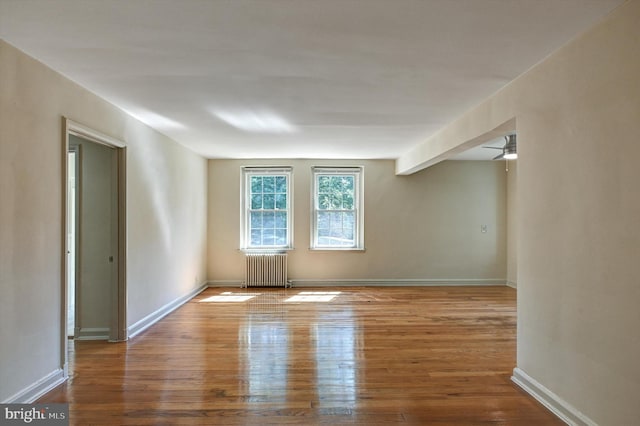 empty room with radiator heating unit, wood-type flooring, beam ceiling, and ceiling fan