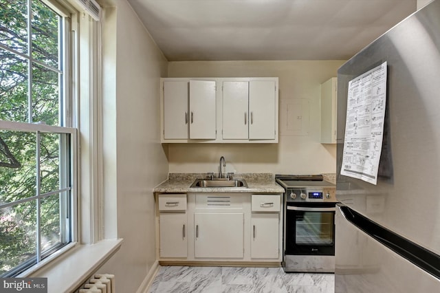 kitchen with appliances with stainless steel finishes, a wealth of natural light, sink, and white cabinets