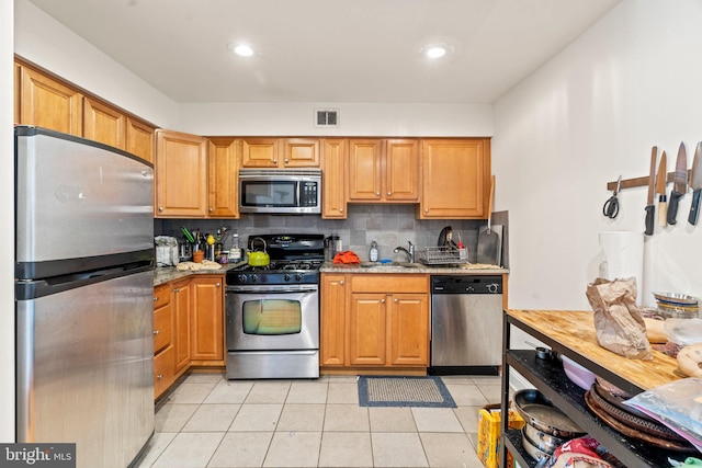 kitchen with light stone counters, sink, stainless steel appliances, backsplash, and light tile patterned floors