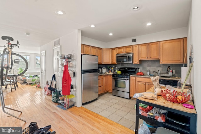 kitchen featuring light wood-type flooring, backsplash, appliances with stainless steel finishes, and sink