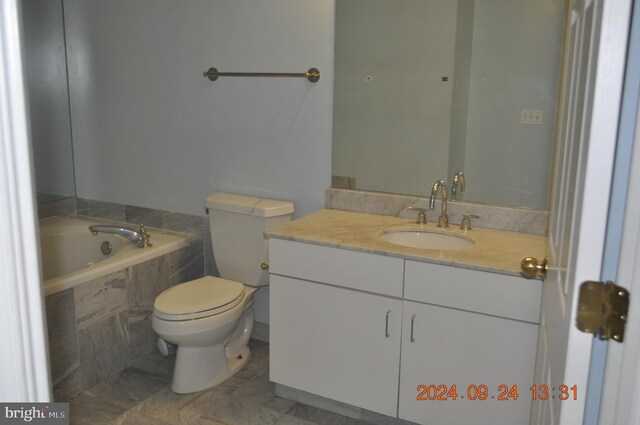 bathroom featuring tiled bath, vanity, and toilet