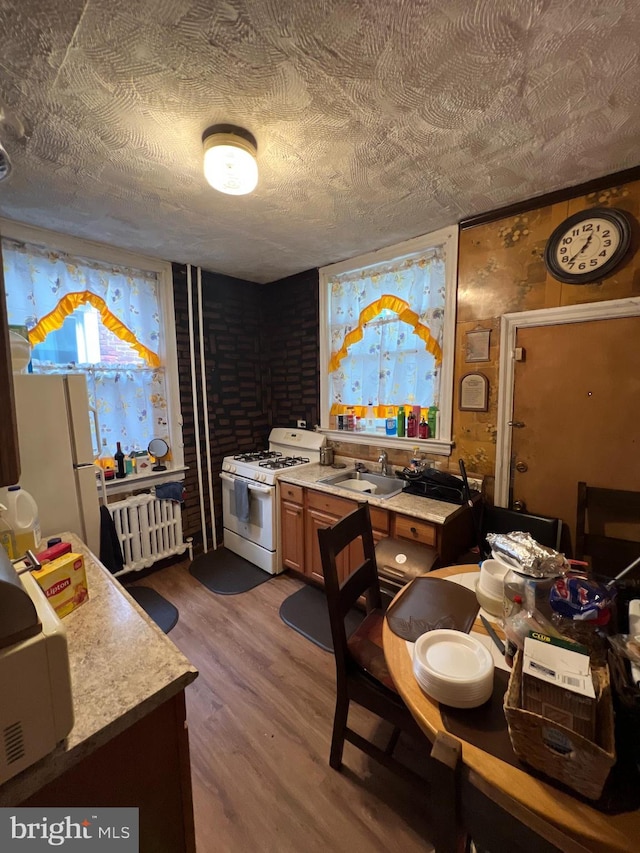 interior space featuring white appliances, a textured ceiling, wood-type flooring, radiator, and sink