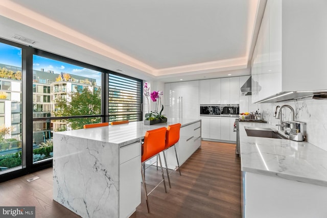 kitchen featuring white cabinetry, sink, backsplash, wood-type flooring, and a kitchen island