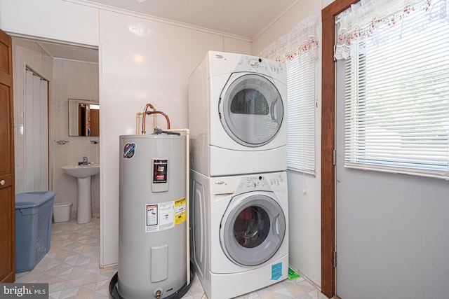 laundry room featuring water heater, crown molding, a healthy amount of sunlight, and stacked washer and clothes dryer