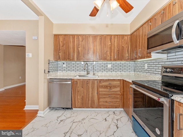 kitchen with light stone countertops, sink, ceiling fan, stainless steel appliances, and tasteful backsplash