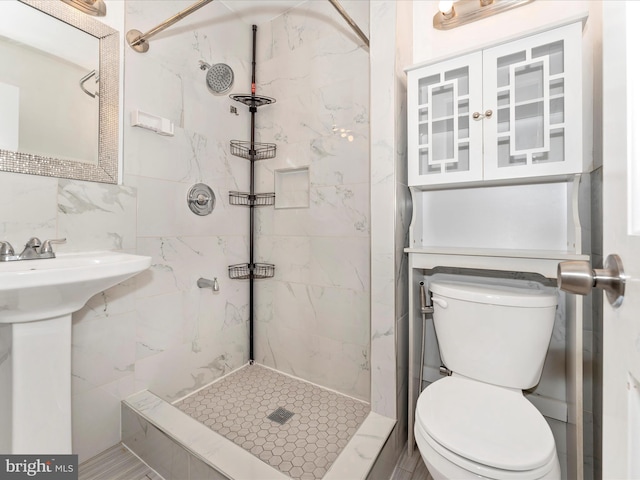 bathroom with toilet, a tile shower, sink, and tile walls