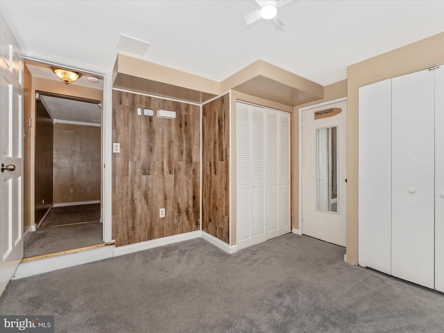 unfurnished bedroom featuring carpet flooring, ceiling fan, wooden walls, and multiple closets