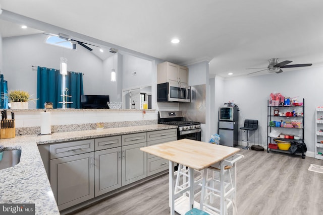 kitchen with light stone counters, ceiling fan, stainless steel appliances, and light hardwood / wood-style flooring